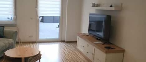 Una sala de estar moderna con suelo de madera, un televisor sobre un mueble y una puerta que da a un espacio al aire libre.