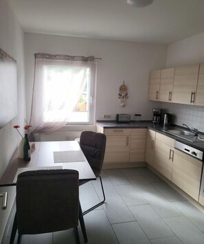 A compact kitchen with a dining area, a window with curtains, and a small decorative item on the wall. - Holiday apartment with 1 bedroom (Bernkastel-Kues)