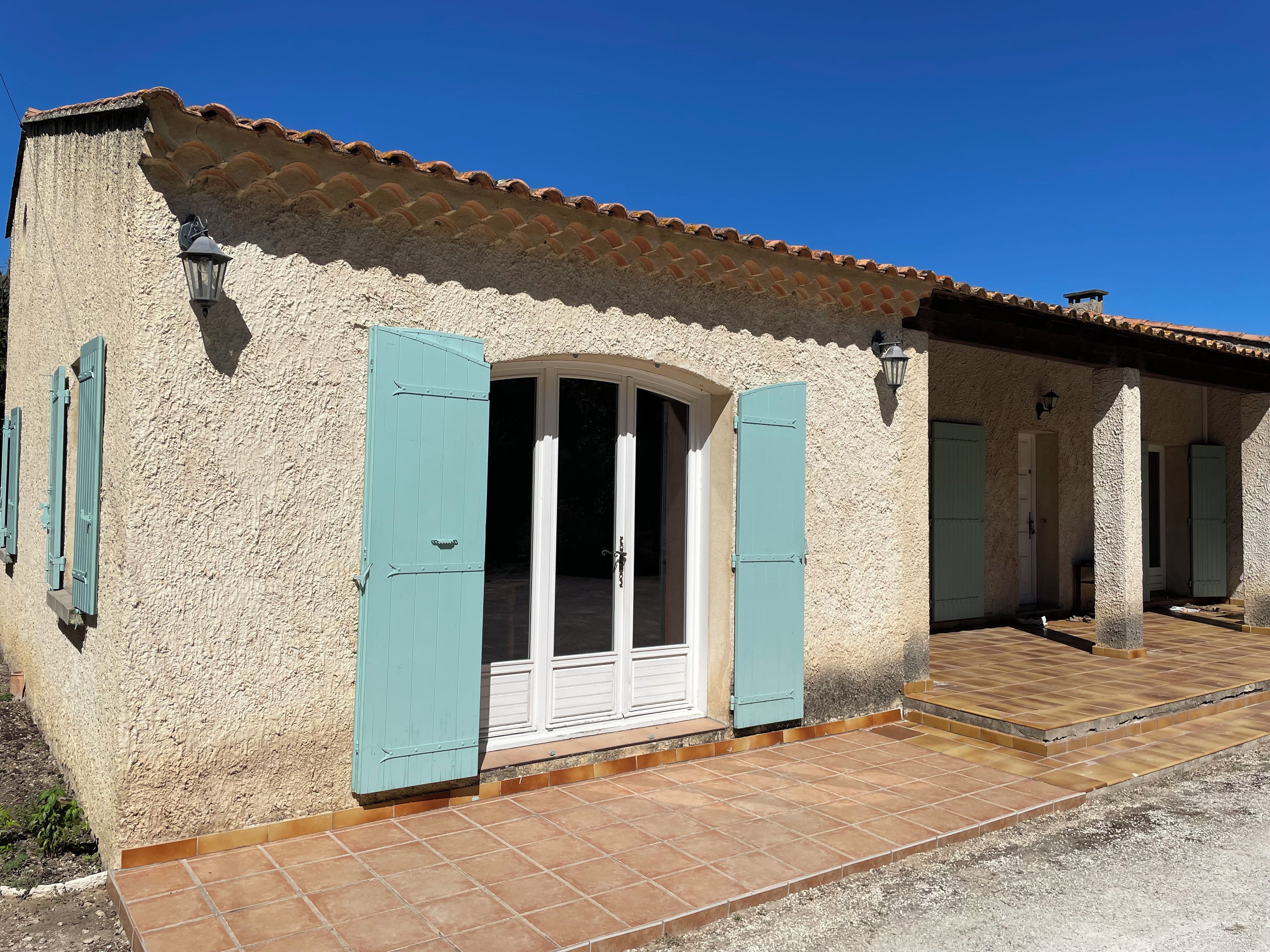 A rustic building with a tiled roof, a doorway with blue shutters, and a tiled entrance.