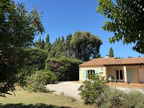 Een landelijk gelegen pand met een huis, voorzien van een pannendak, een grindpad en veel groen, zoals bomen en struiken.
