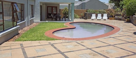A swimming pool with a curved edge, surrounded by a patio with patterned tiles.