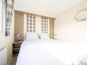 A bedroom with a bed, two bedside tables, a nightstand, a window with curtains, and a wall-mounted mirror. - Riverside Chalet Escape in Kerkdriel (Kerkdriel)