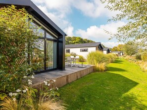 A modern house with a glass facade, a wooden deck, and a well-maintained lawn. - Riverside Chalet Escape in Kerkdriel (Kerkdriel)