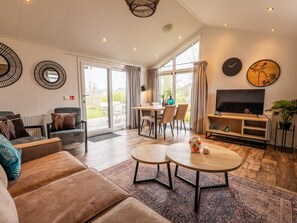 A modern living room with a sofa, coffee table, TV, and dining area. - Riverside Chalet Escape in Kerkdriel (Kerkdriel)
