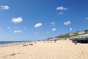 A beach with a clear sky, sandy shore, and a row of beach huts. - Holiday apartment with 2 bedrooms (Dishoek)