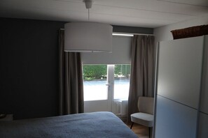 A hotel room with a bed, a chair, a large window, and a ceiling light fixture. - Holiday apartment with 2 bedrooms (Dishoek)
