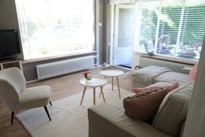 A living room with a sofa, a chair, two small tables, a radiator, and a television. - Holiday apartment with 2 bedrooms (Dishoek)