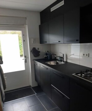 A compact kitchen with dark cabinets, a stainless steel sink, and a gas stove. - Holiday apartment with 2 bedrooms (Dishoek)