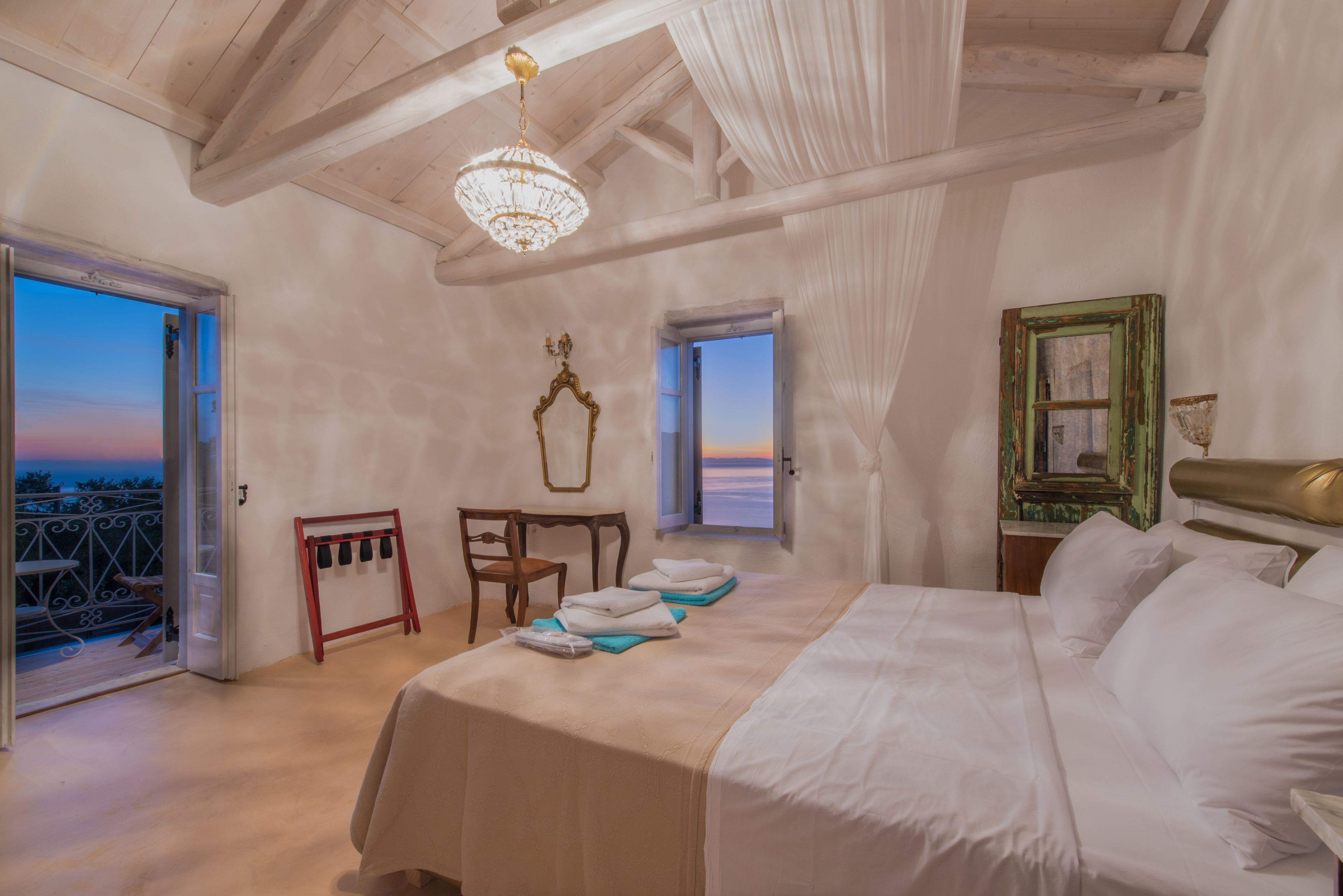 A bedroom with a bed, a chair, a table, a mirror, and two windows.