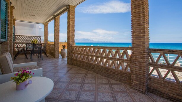 Un espacio al aire libre techado con vistas al mar, que incluye una mesa con sillas, una planta en maceta y una valla de madera.