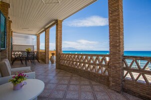 Un espacio al aire libre techado con vistas al mar, que incluye una mesa con sillas, una planta en maceta y una valla de madera.
