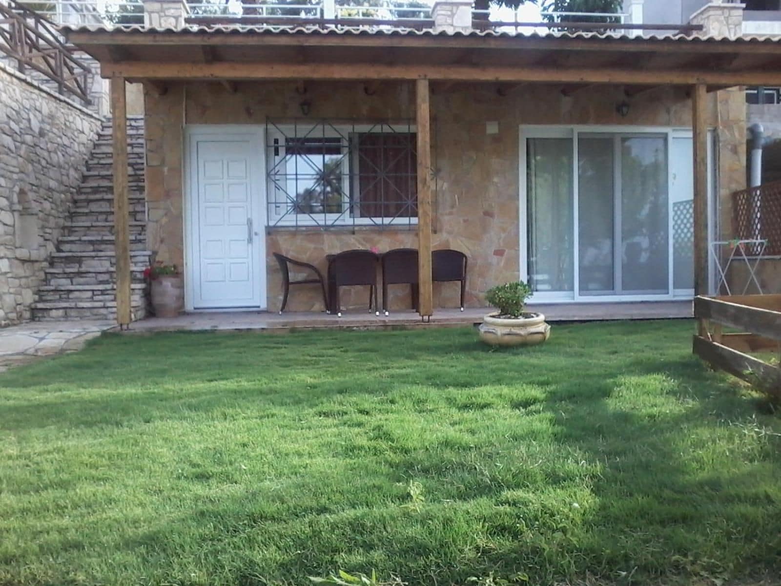 A house with a stone exterior, a covered patio with chairs, and a small lawn.
