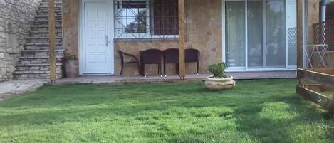 A house with a stone exterior, a covered patio with chairs, and a small lawn.