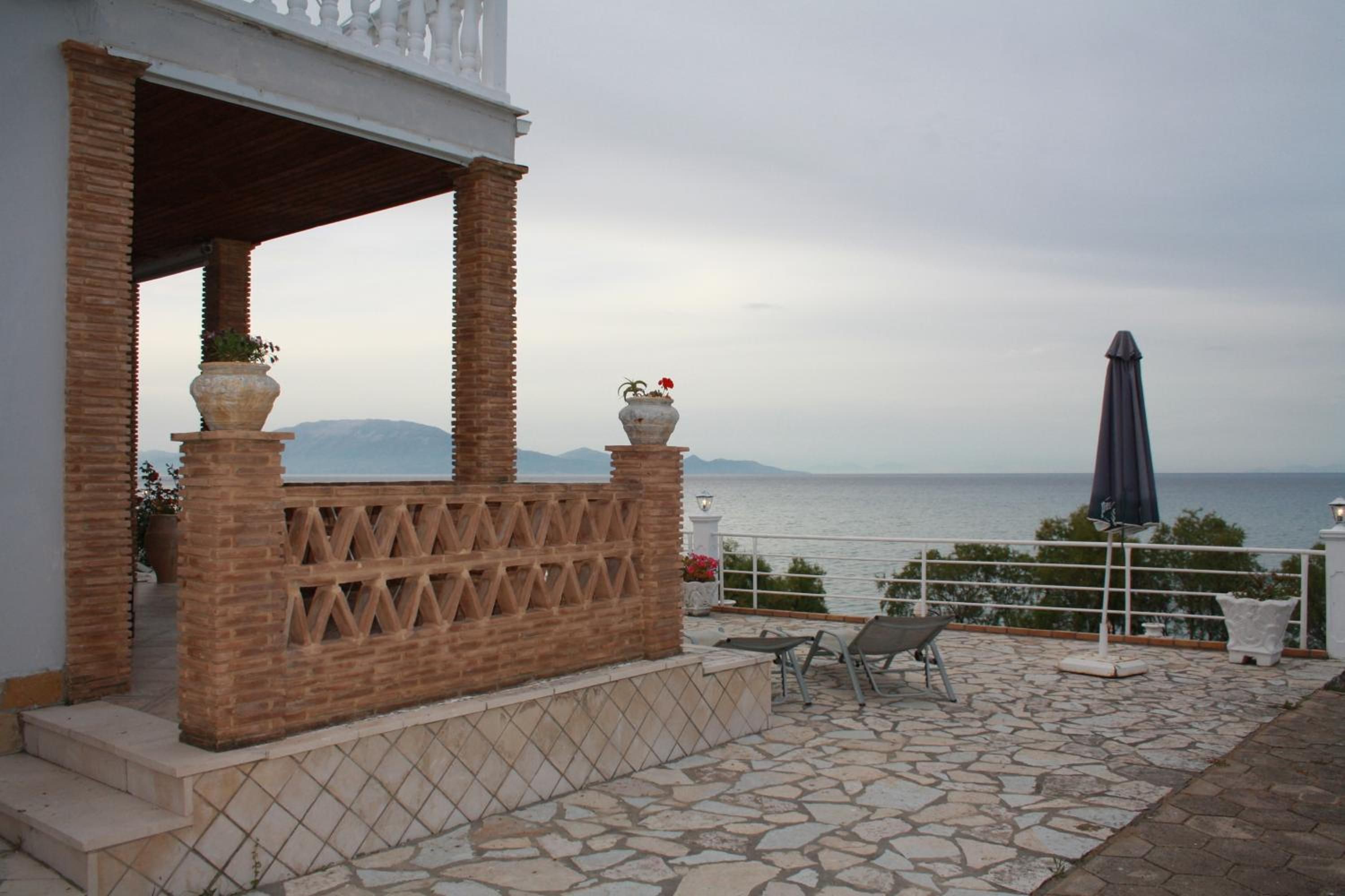 A terrace with stone flooring, a white railing, and a view of the sea.