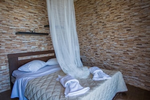 Uma cama de solteiro com cabeceira de madeira, um dossel branco pendurado e parede com padrão de tijolos.
