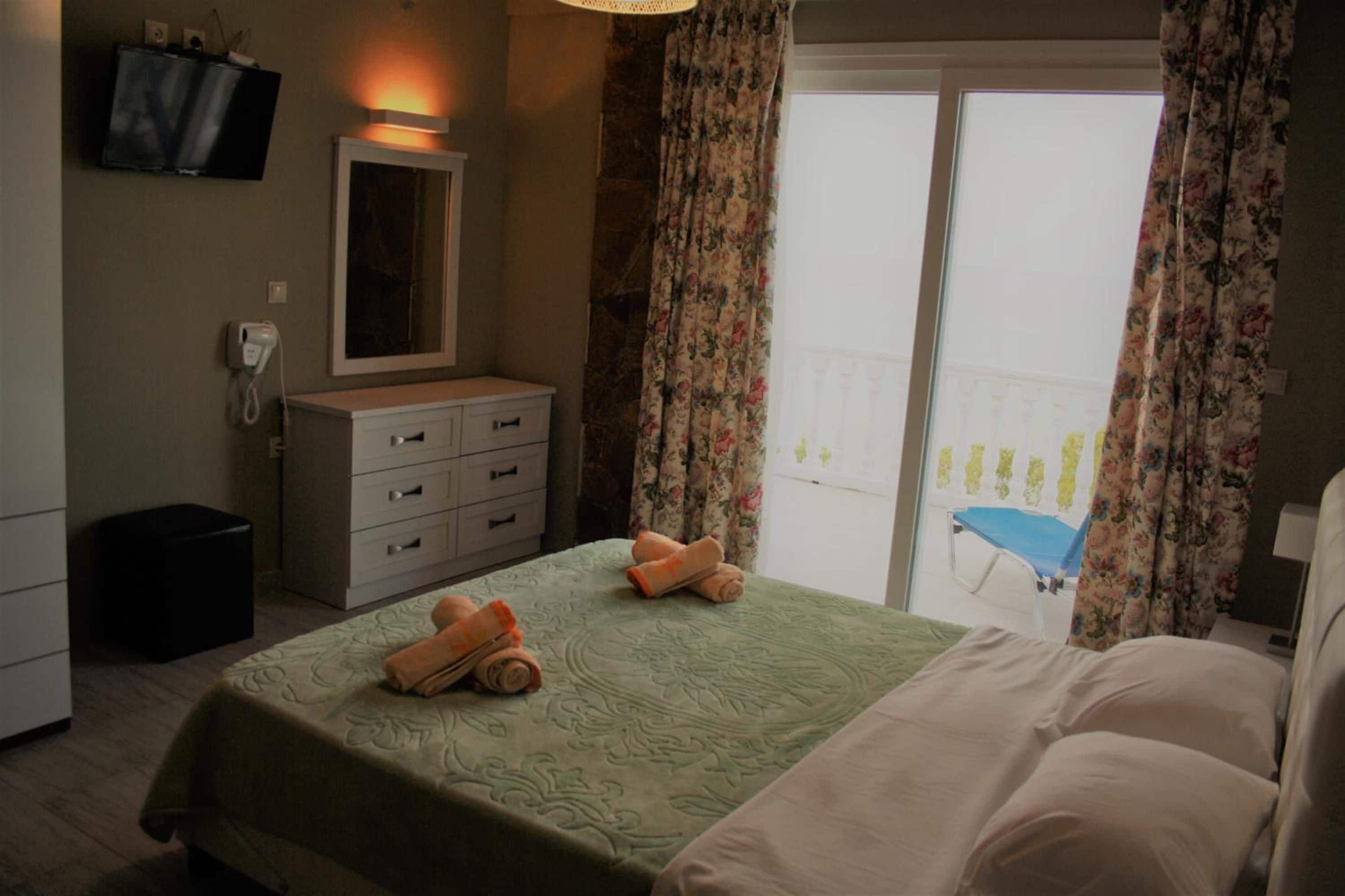 A hotel room with a bed, a bedside table, a mirror, a telephone, and a balcony with a chair.