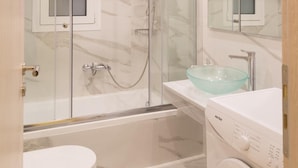 Un baño moderno con ducha envuelta en vidrio, un lavamanos blanco con lavabo de vidrio y una lavadora.