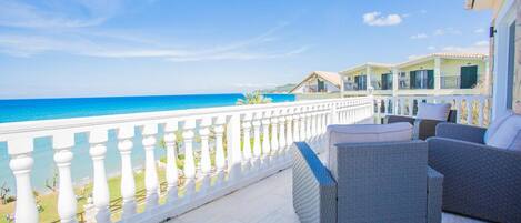A balcony with a view of the sea, white balustrades, and outdoor furniture.