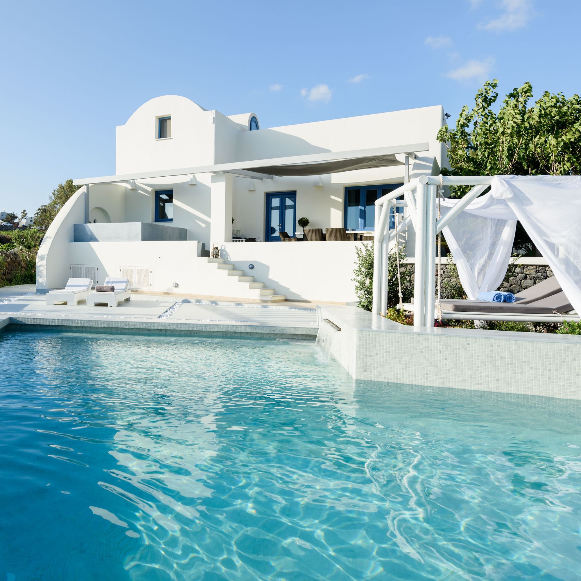 A modern white villa with a pool, a covered outdoor seating area, and a staircase leading to a balcony.