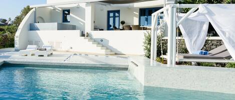 A modern white villa with a pool, a covered outdoor seating area, and a staircase leading to a balcony.