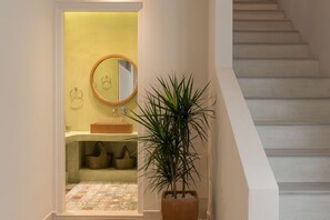 Una escalera conduce a un baño con una pared amarilla, un espejo redondo y una planta en maceta.