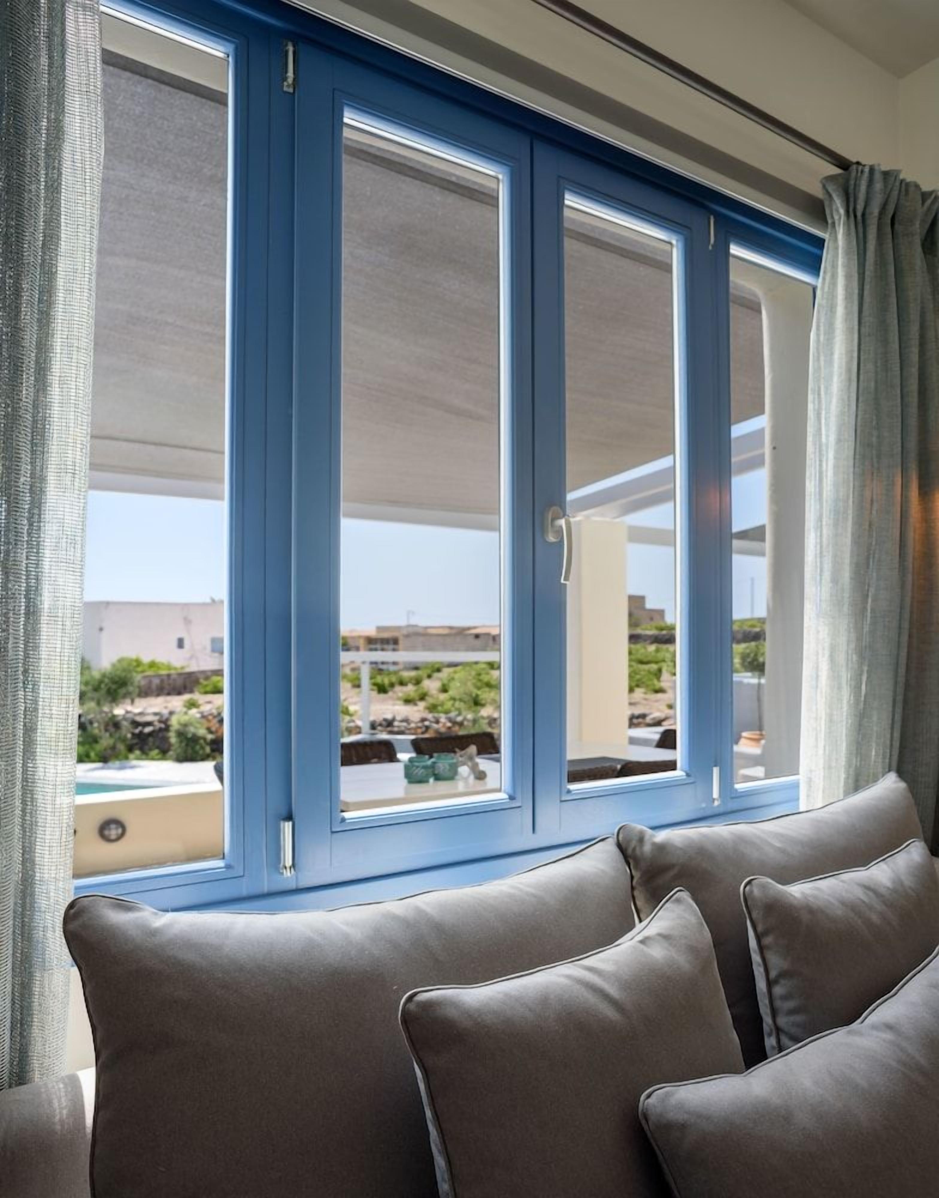 A room with a blue-framed window, a grey sofa, and a view of a pool and buildings outside.