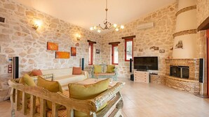 Una sala de estar con paredes de piedra, un conjunto de sofá de madera, un televisor y una chimenea.