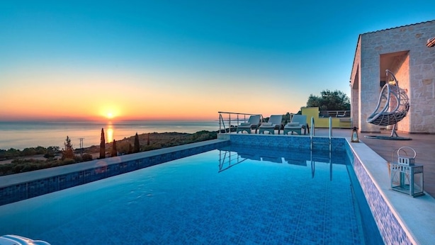 Una piscina con vista al atardecer, sillas de descanso y un edificio de piedra con una escultura original.