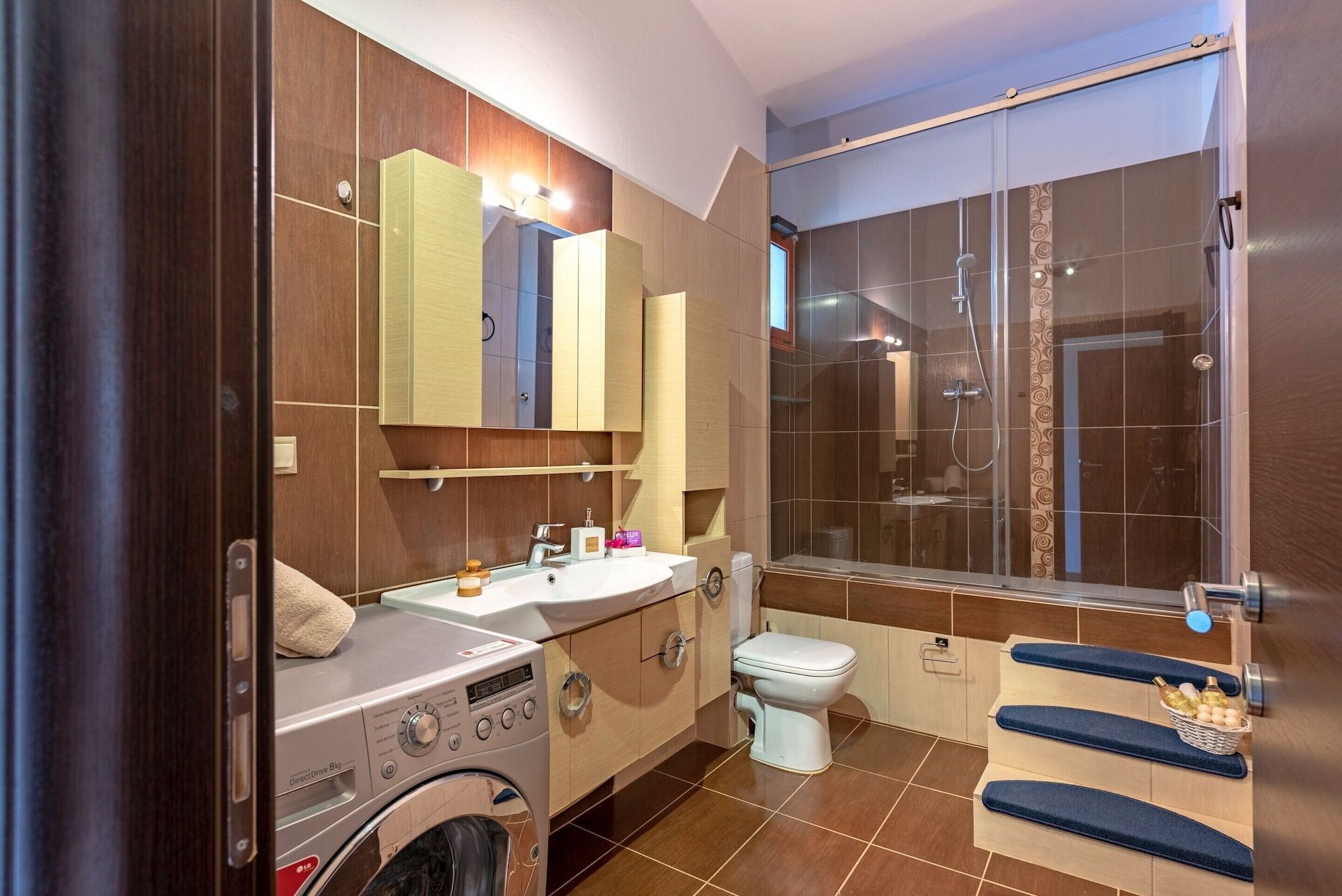 A modern bathroom with a built-in washer, a toilet, a sink, and a shower enclosure.