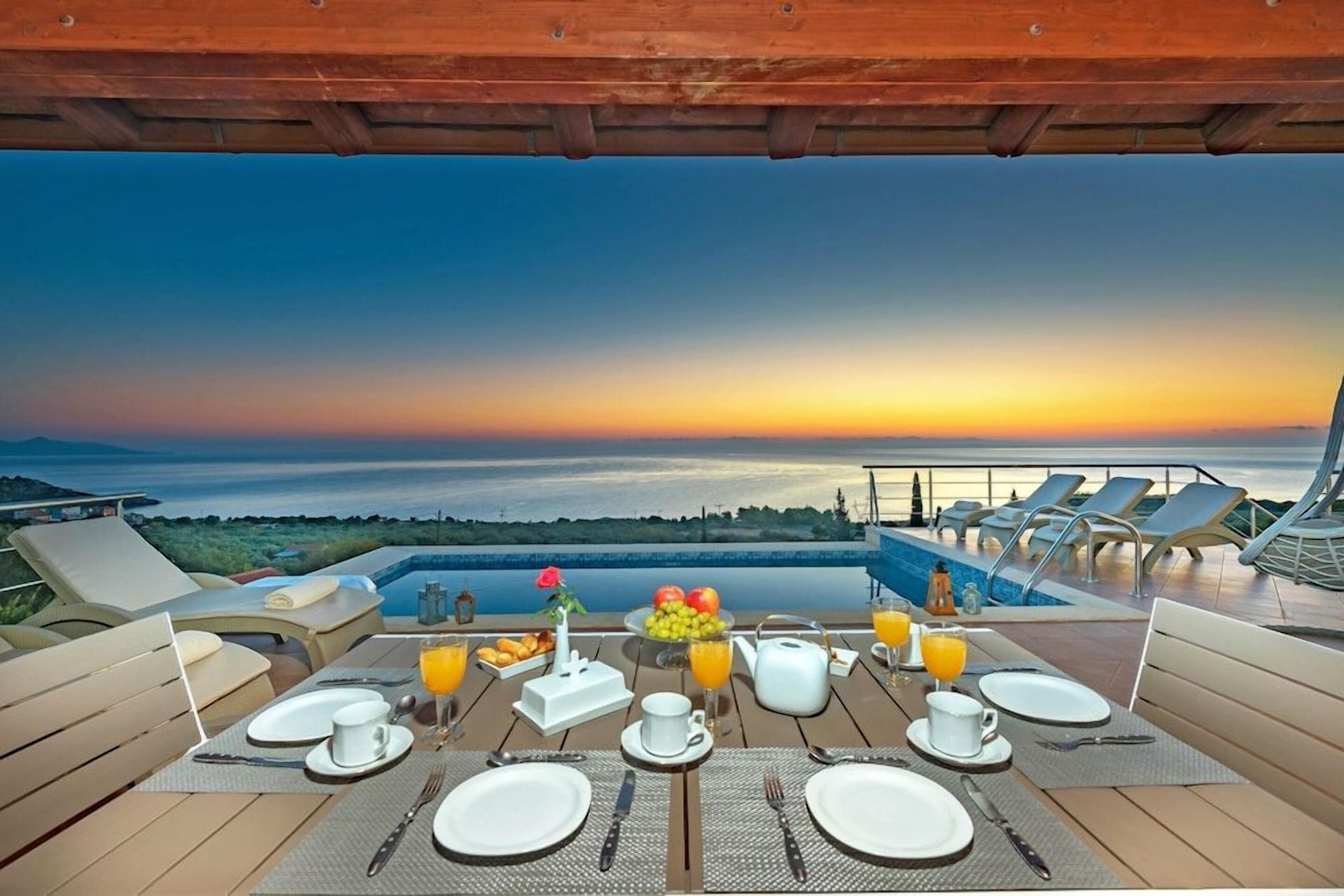 A dining table set for breakfast with a view of the ocean at sunset.