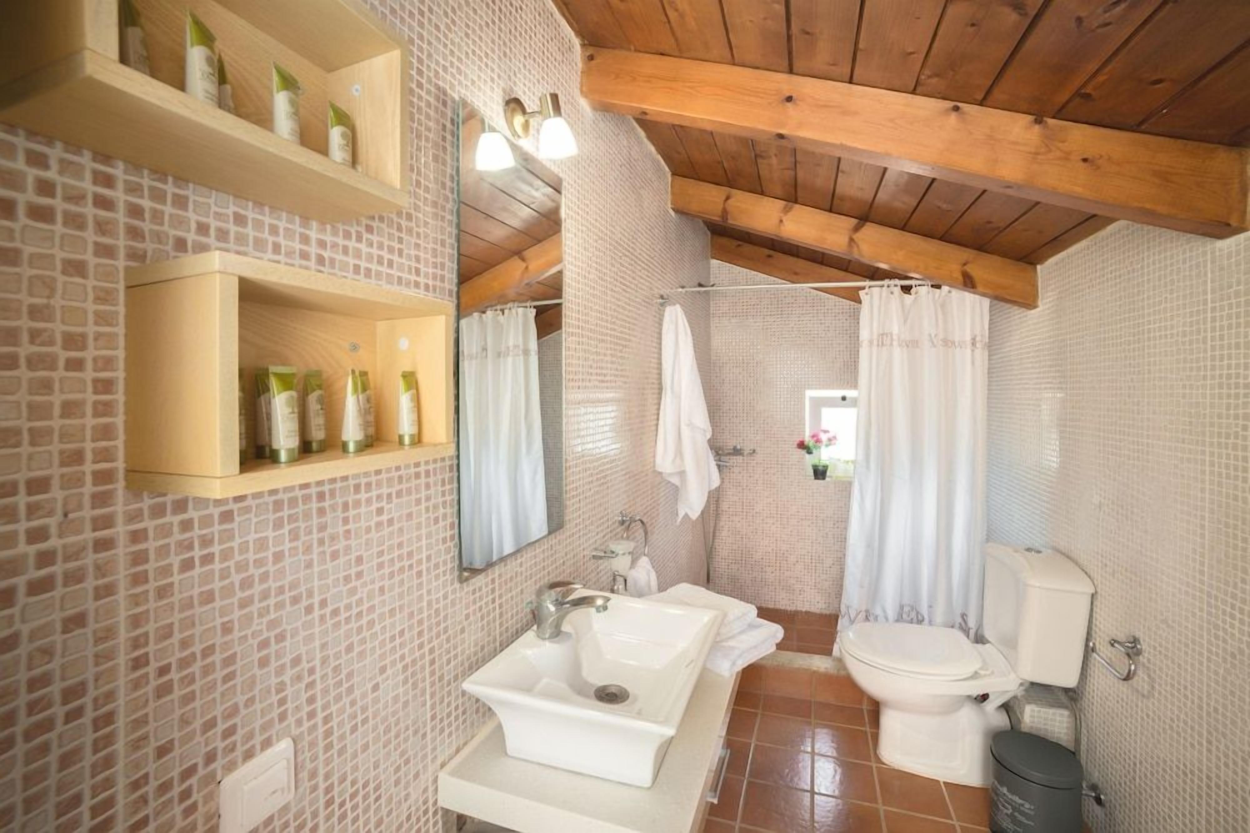 A bathroom with a tiled backsplash, a wooden ceiling, a sink, a toilet, and a shower curtain.