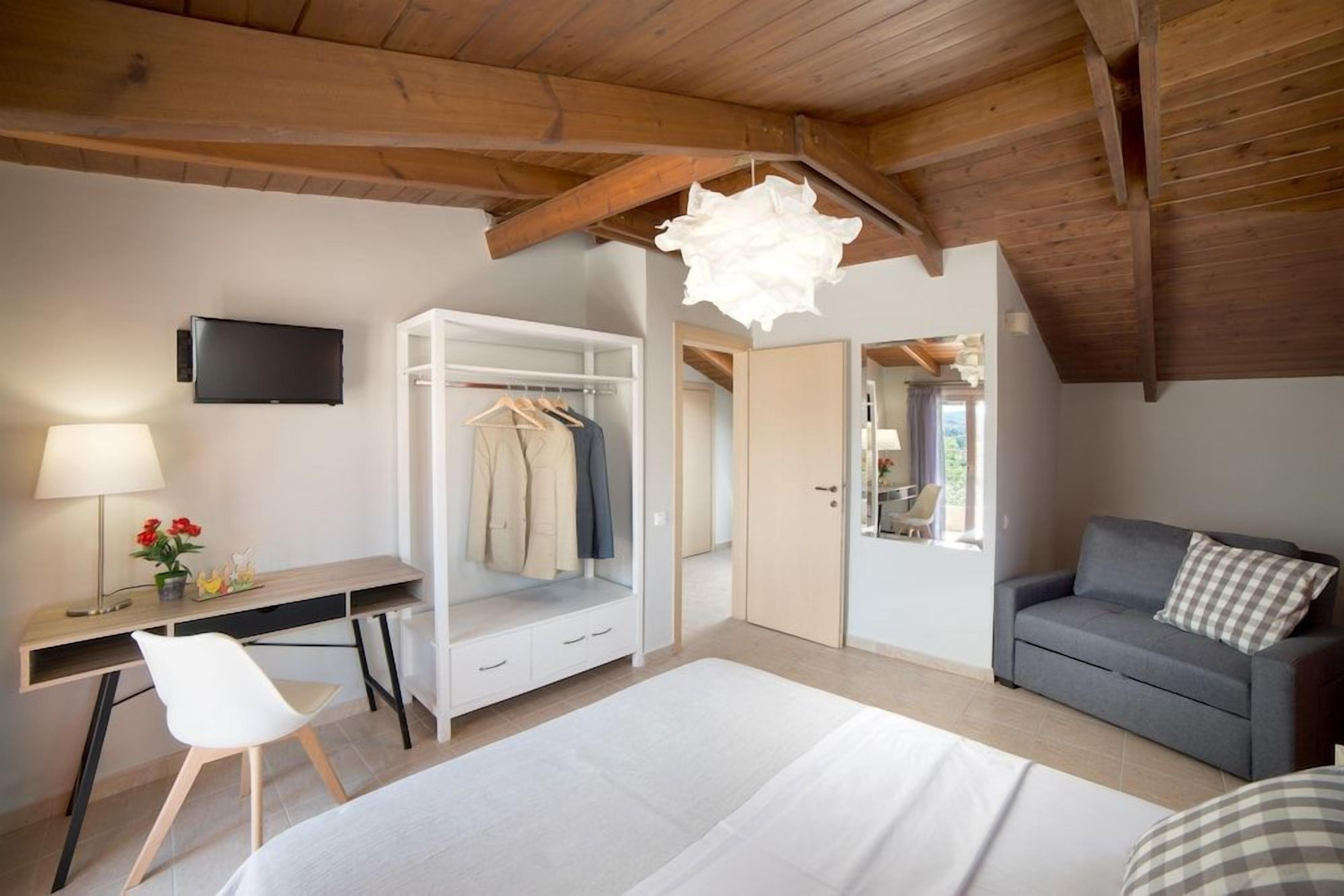 A bedroom with a bed, a desk, a chair, a wardrobe, a grey sofa, and a television.