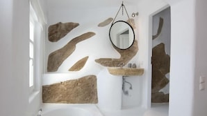 A modern bathroom with a freestanding bathtub, a stone wall, and a round mirror. - Villa Azurite (Mykonos)