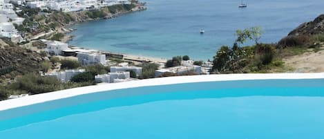 A coastal view with a swimming pool, white buildings, and boats on the water.