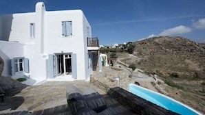 A white building with a stone pool and a view of a rocky hillside. - Villa Azurite (Mykonos)