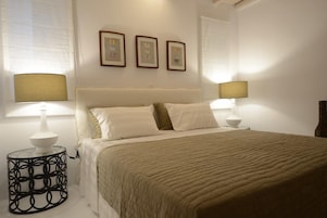 Un dormitorio con una cama, dos lámparas de noche, una mesita redonda y tres cuadros en la pared.