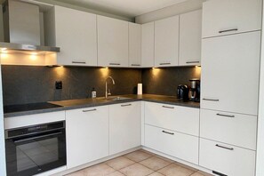 A modern kitchen with white cabinets, a black countertop, and a built-in oven. - Holiday home with 1 bedroom (Julianadorp)