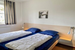 A room with two beds, a window with curtains, a wall-mounted picture, and bedside lamps. - Holiday home with 1 bedroom (Julianadorp)