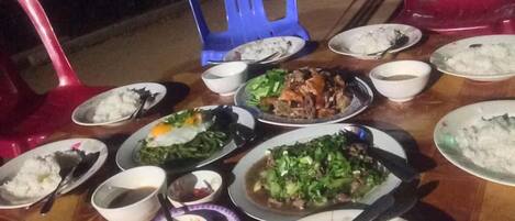 A table set with various dishes, including rice and vegetables, in a dining area with plastic chairs.