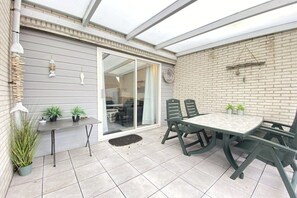 Eine Terrasse mit Tisch, Stühlen, Blumentöpfen und einer Schiebetür zu einem Innenbereich.