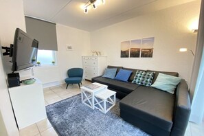 Un salon moderne avec un canapé, un téléviseur, une petite table et un fauteuil.