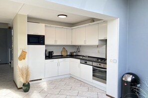 A modern kitchen with white cabinets, a black microwave, and stainless steel appliances. - Holiday home with 3 bedrooms (Julianadorp aan Zee)