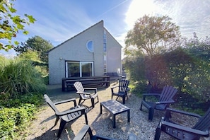 A modern building with a brick exterior, a large window, and outdoor seating with Adirondack chairs and a table. - Holiday home with 3 bedrooms (Julianadorp aan Zee)