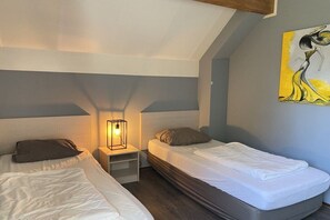 Een slaapkamer met twee bedden, een nachtkastje met een lamp en een schilderij aan de muur.