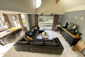 A modern living room with a sectional sofa, a dining area with a wooden table and chairs, a kitchen with a TV, and a sliding glass door to an outdoor patio. - Holiday home with 3 bedrooms (Julianadorp aan Zee)
