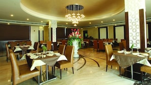 A hotel dining area with round tables, chairs, and a central floral arrangement. - Wingston Goverdhan (Mathura)