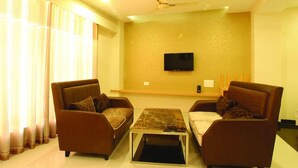 A living room with two sofas, a coffee table, a flat-screen TV mounted on the wall, and a ceiling fan. - Wingston Goverdhan (Mathura)
