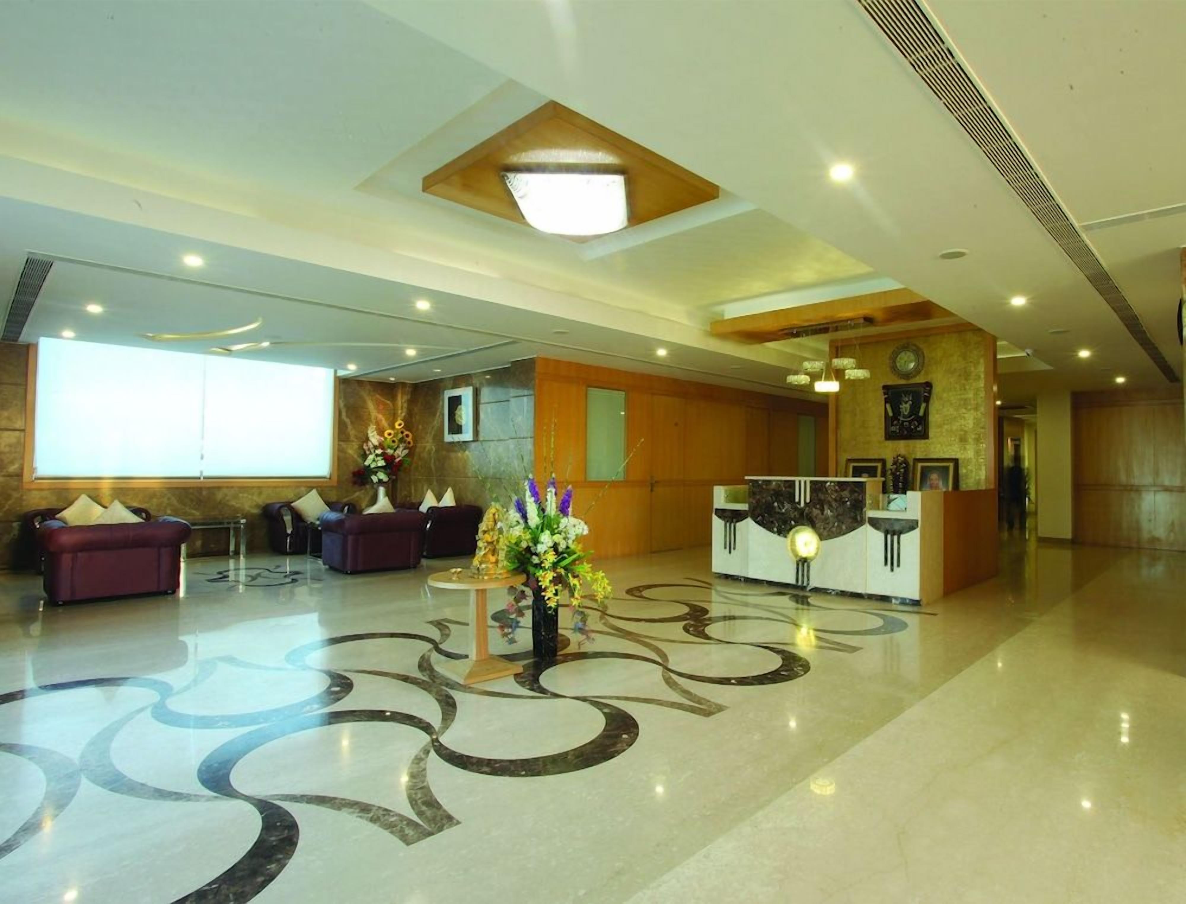 A hotel lobby with a reception desk, seating area, and a decorative vase with flowers.