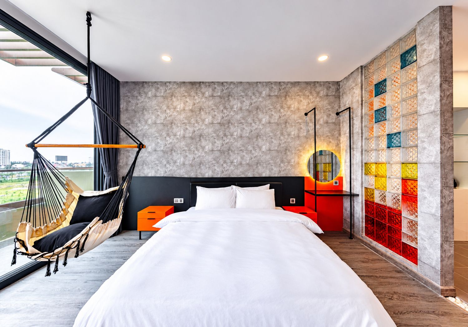 Habitación de hotel con una cama grande, una hamaca, vistas a la ciudad y una pared colorida.
