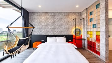 Habitación de hotel con una cama grande, una hamaca, vistas a la ciudad y una pared colorida.